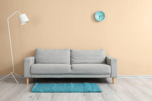 Elegante sofá gris con lámpara y reloj colgando en la pared beige en la habitación - Foto, imagen