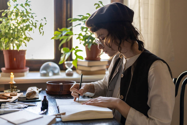 Keskittynyt kuvittaja taiteilija nuori nainen kiinnittää kannettavan viihtyisässä työpajassa freelance järjestyksessä. Suunnittelija tyttö suorittaa kuvia istuessaan pöydässä taidestudiossa vihreitä kasveja. Innoitustyö - Valokuva, kuva