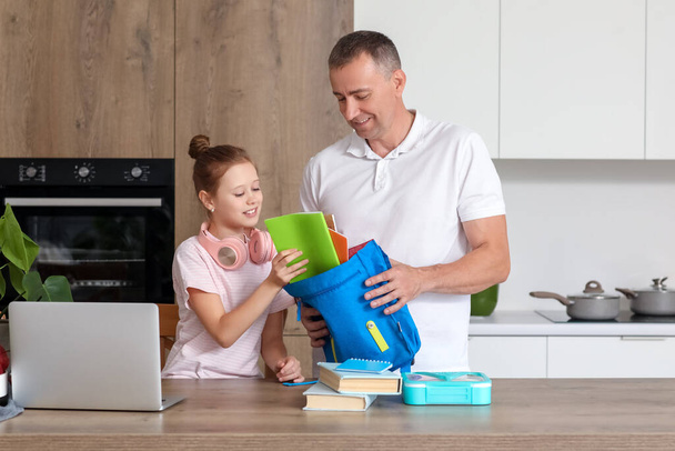 Батько допомагає своїй маленькій доньці упакувати шкільну сумку на кухню - Фото, зображення