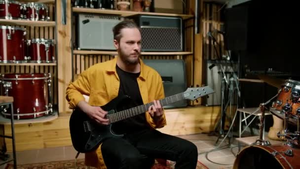 πορτρέτο του νεαρού ροκ καλλιτέχνη με ηλεκτρική κιθάρα στο στούντιο ηχογράφησης παίζει το δικό του κομμάτι μουσικό όργανο ντραμς φόντο - Πλάνα, βίντεο
