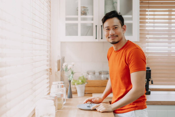 Asian man preparing his easy breakfast in the kitchen in warm light morning. - Photo, image