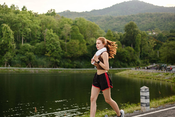 Mujer asiática sana está corriendo corriendo al aire libre. Deportiva corriendo. Ejercicio femenino en el parque al aire libre. Puesta o salida del sol. Foto de alta calidad - Foto, Imagen