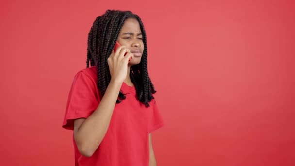 Kızgın Afrikalı kadın stüdyoda kırmızı arka planlı cep telefonuyla konuşuyor. - Video, Çekim