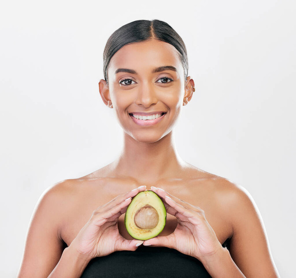 Woman, beauty and avocado in studio portrait for health, wellness and diet for facial glow by white background. Girl, model and healthy skin with fruit, makeup or cosmetics for self care with smile. - Foto, afbeelding