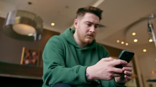 een gast bij de receptie van het hotel houdt een telefoon in zijn handen, sms 'en met iemand die wacht op check-in het concept gastvrijheid en technologie - Video