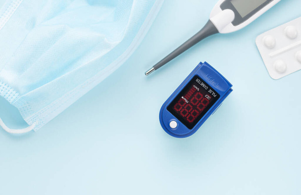 Medical kit for the prevention and treatment of coronavirus. Mask, test, pulse oximeter and medication on a blue background. - Фото, зображення