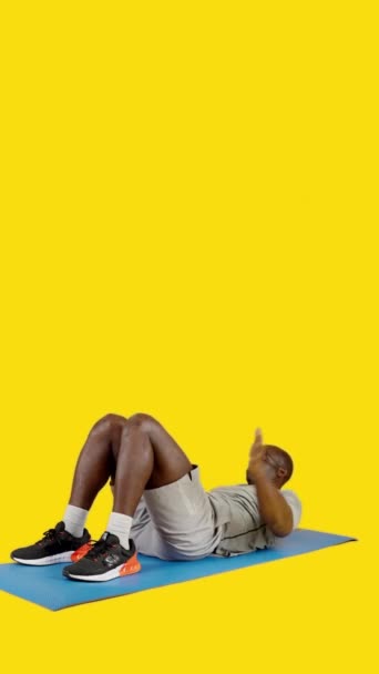 Video in studio con sfondo giallo di un uomo africano su un tappeto facendo roll up esercizio - Filmati, video