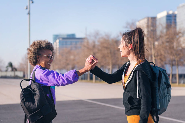 Porträt zweier glücklicher Sportlerinnen beim Händeschütteln vor dem Stadtlauf, Konzept der Freundschaft und des sportlichen Lebensstils - Foto, Bild