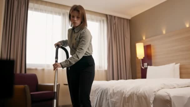młoda dziewczyna sprzątaczka w hotelu dziewczyna sprzątanie pokój odkurzanie dywan w luksusowym koncepcji pokoju czystość i gościnność - Materiał filmowy, wideo