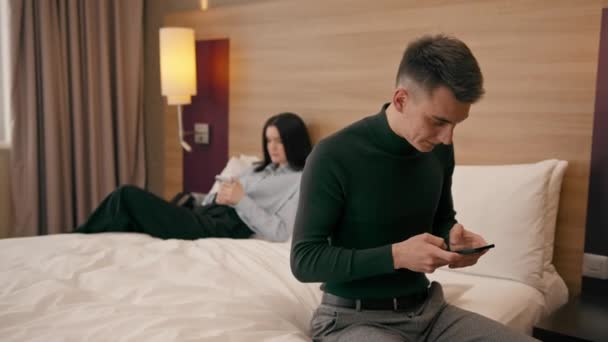 νεαρό ζευγάρι στο δωμάτιο ενός πολυτελούς ξενοδοχείου οι άνθρωποι κρατούν smartphones στα χέρια τους δεν επικοινωνούν μεταξύ τους ταξίδια - Πλάνα, βίντεο