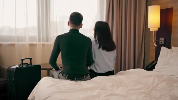 giovane coppia nella stanza di un hotel di lusso gli amanti delle camere cadono sul letto alzano le mani verso l'alto vista posteriore concetto di viaggio - Filmati, video