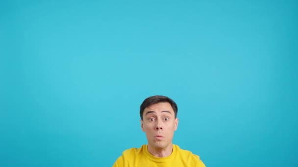 Video in studio with blue background of a shocked caucasian man pointing up with surprised look - Footage, Video
