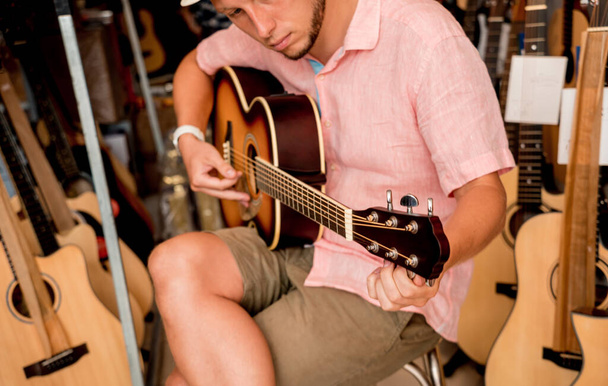 若い音楽家がギターショップでクラシックギターをチューニング. - 写真・画像