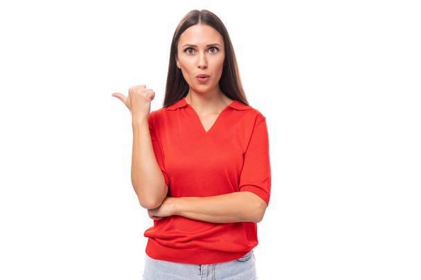 retrato de uma jovem morena europeia bonita em uma camiseta vermelha ativamente gesticulando com o dedo indicador em direção à parede. - Foto, Imagem