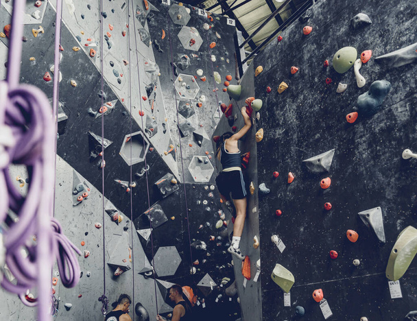 Strong woman on artificial climbing wall with colorful grips and ropes. - Foto, Bild