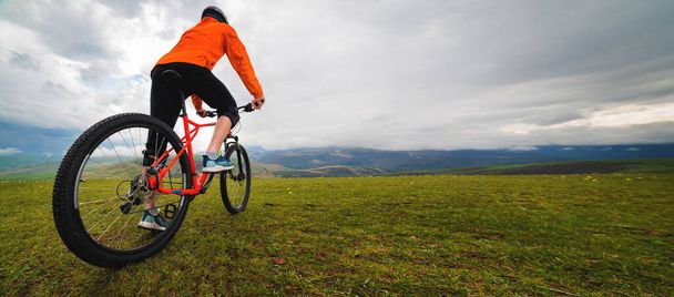 Cycling. A man on an enduro bike stands in a landscape in the mountains, rear view from below. Outdoor sports. - Foto, immagini