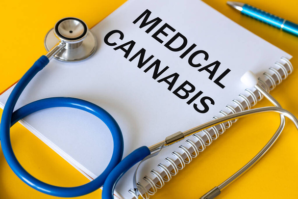 Stéthoscope médical, cahier blanc avec l'inscription Cannabis médical, beau fond jaune, La consommation de cannabis et de marijuana en médecine - Photo, image