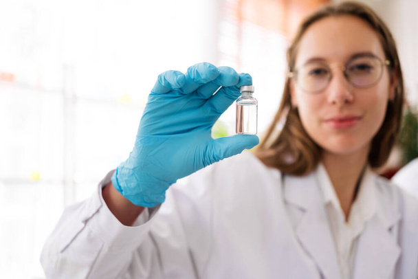 Caucasian woman scientist researcher looking and holding a small Medium glass bottle for chemical analysis of liquids in the lab. Scientist working with chemical equipment in the lab. - Photo, Image