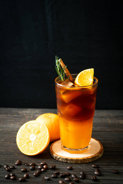 A glass of iced americano black coffee and layer of orange and lemon juice decorated with rosemary and cinnamon - Foto, Bild