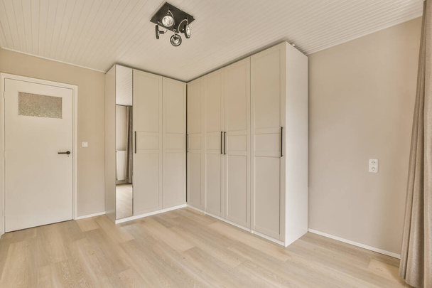 een lege kamer met houten vloeren en witte kasten aan weerszijden van de kamer, is er een armatuur in de - Foto, afbeelding
