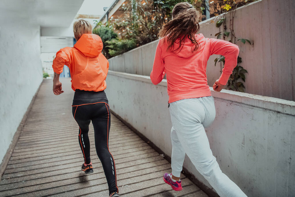 Two women in sports clothes running in a modern urban environment. The concept of a sporty and healthy lifestyle.  - Photo, image