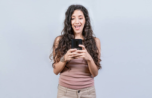Happy and surprised girl looking at a promotion on the cell phone. Smiling woman texting with cell phone isolated. Happy latin girl using cell phone isolated - Valokuva, kuva
