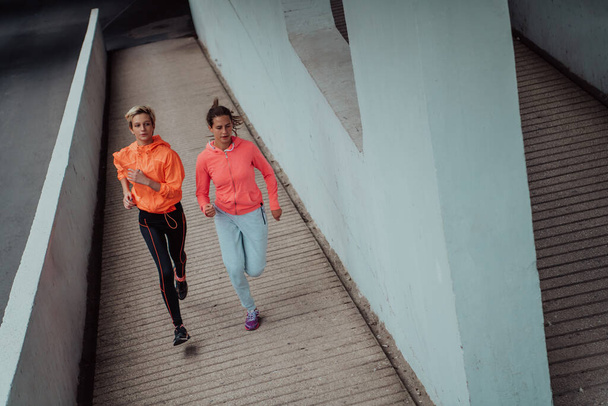 現代の都会の中を走るスポーツウェアを着た2人の女性。スポーティーで健康的なライフスタイルのコンセプト.  - 写真・画像
