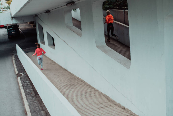Two women in sports clothes running in a modern urban environment. The concept of a sporty and healthy lifestyle.  - 写真・画像