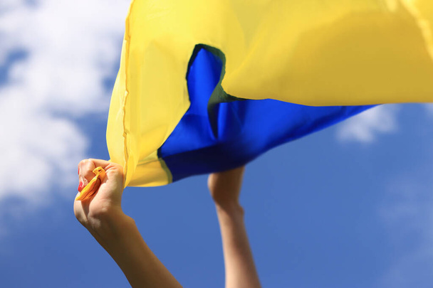 Ruce žen s ukrajinskou vlajkou proti obloze. Ukrajinská vlajka vlaje ve větru. Den nezávislosti Ukrajiny. Žlutomodrá vlajka - Fotografie, Obrázek