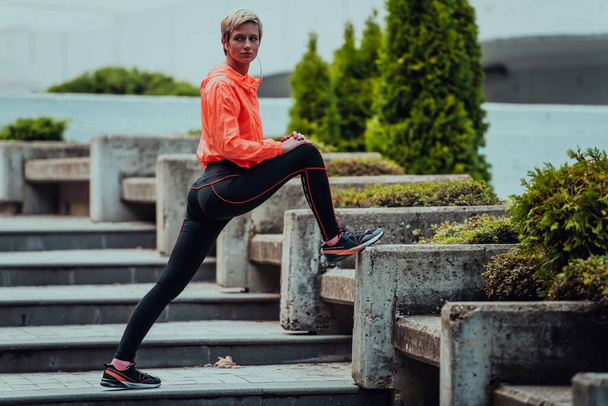 Fit attractive woman in sportswear stretching one leg before jogging on the footpath outdoor in summer among greenery. Workout, sport, activity, fitness, vacation and training conept - Foto, Bild
