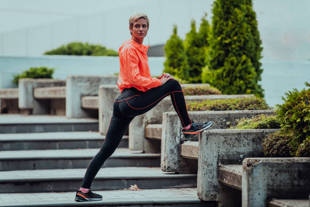 Fit attractive woman in sportswear stretching one leg before jogging on the footpath outdoor in summer among greenery. Workout, sport, activity, fitness, vacation and training conept - 写真・画像