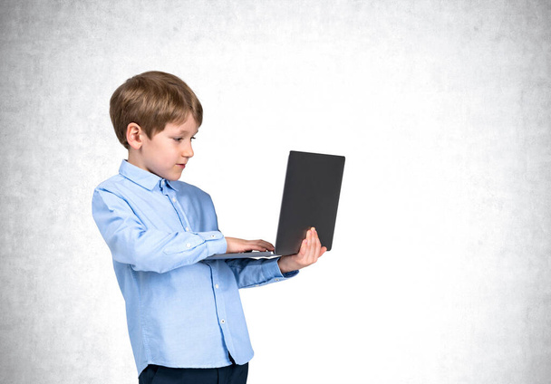 Child boy using laptop and browse internet, portrait profile on empty copy space grey concrete background. Concept of online studies and e-learning - Photo, Image
