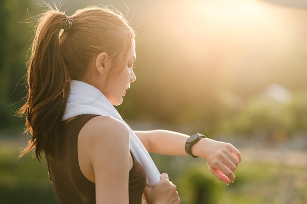 Gesunde Frau entspannen Sie sich nach der Abkühlung und schauen Smart Watch für Check-Timing-Lauf. Frauentraining nach der Fitness- und Joggingeinheit im Park. Gesundes und Lifestyle-Konzept. Hochwertiges Foto - Foto, Bild
