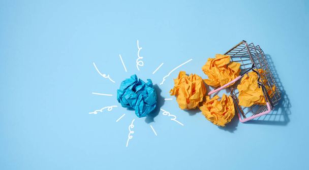 Bolas de papel arrugadas sobre un fondo azul y una cesta de la compra. Concepto de una nueva idea - Foto, Imagen