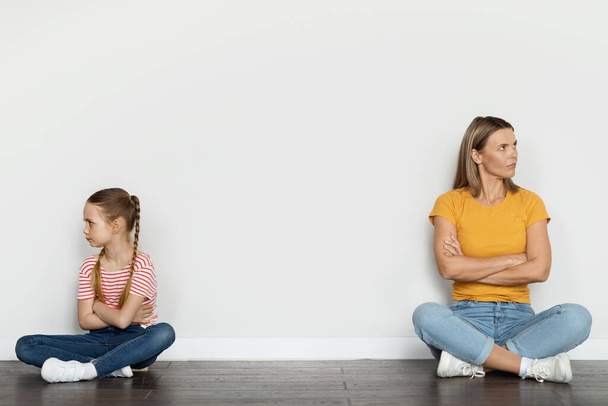 Portret van beledigde jonge moeder en haar dochtertje zitten op de vloer in de buurt van de Witte Muur en negeren elkaar, moeder en kind lijden misverstand na ruzie thuis, kopiëren ruimte - Foto, afbeelding