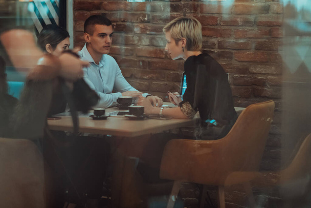 Photo through the glass of a group of business people sitting in a cafe and discussing business plans and ideas for new online commercial services.  - Φωτογραφία, εικόνα