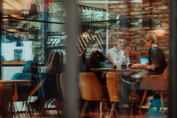 Photo through the glass of a group of business people sitting in a cafe and discussing business plans and ideas for new online commercial services.  - 写真・画像