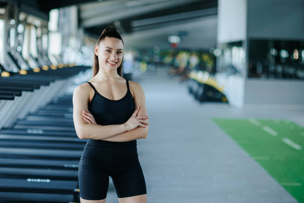 captivating gym portrait, an athletic young woman exudes confidence as she strikes a pose, showcasing her fitness prowess. Her radiant smile and joyful expression reflect her satisfaction - 写真・画像
