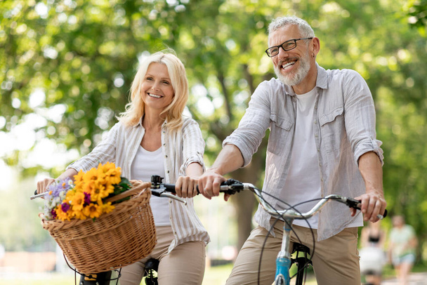 Portret szczęśliwej dojrzałej pary jeżdżącej na rowerach w parku letnim, wesoły starszy małżonek bawiący się razem na świeżym powietrzu, uśmiechnięty starszy mężczyzna i kobieta cieszący się wolnym czasem na emeryturze, zbliżenie - Zdjęcie, obraz