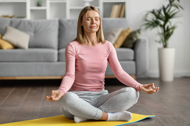 Meditation Concept. Beautiful Calm Woman Meditating At Home In Lotus Position, Peaceful Young Caucasian Lady Practicing Yoga, Sitting With Closed Eyes On Fitness Mat In Light Room, Copy Space - Foto, Imagem