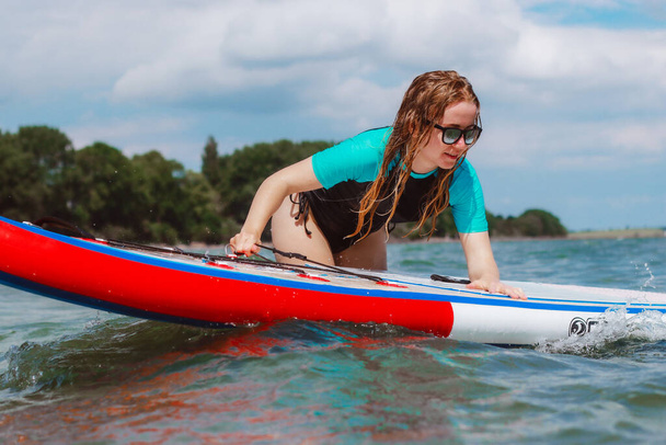 Een jonge vrouw duwt een sup board in de zee. Gezond en fit leven in het natuurconcept.  - Foto, afbeelding