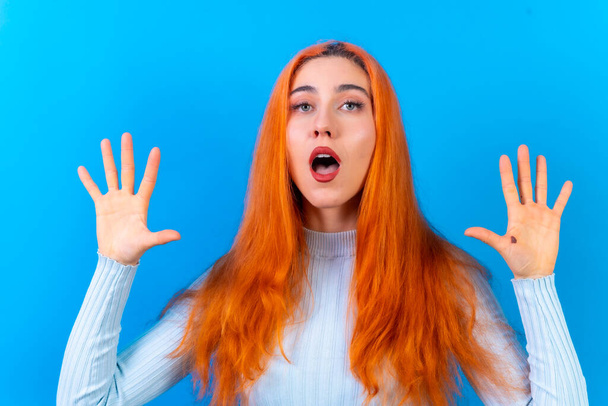 Red-haired woman in studio photography making the astonished gesture on a blue background - 写真・画像