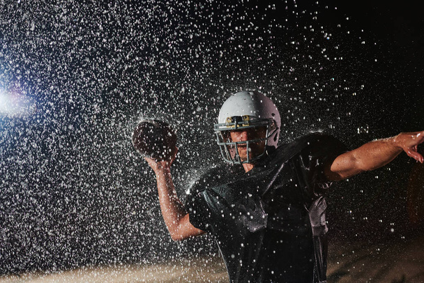 American Football Field: Lonely Athlete Warrior Standing on a Field Holds his Helmet and Ready to Play. Player Preparing to Run, Attack and Score Touchdown. Rainy Night with Dramatic Fog, Blue Light. - Φωτογραφία, εικόνα