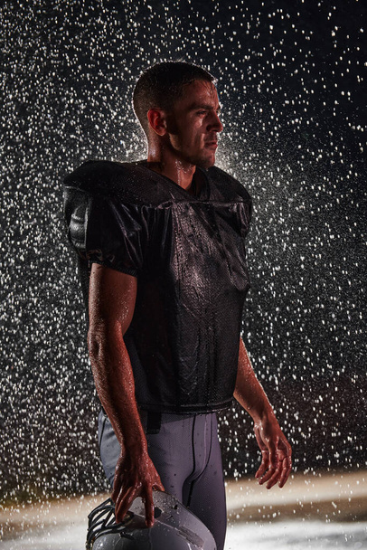 American Football Field: Lonely Athlete Warrior Standing on a Field Holds his Helmet and Ready to Play. Player Preparing to Run, Attack and Score Touchdown. Rainy Night with Dramatic Fog, Blue Light. - Фото, изображение