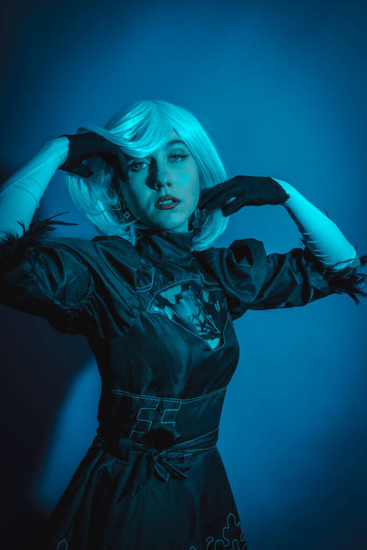 Portrait of cosplay woman in black costume and a white wig in studio with blue led light - Photo, image
