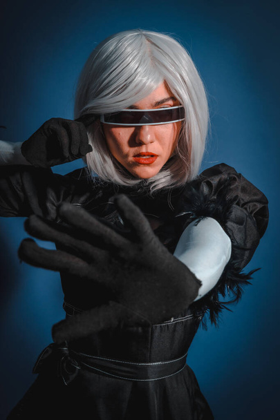 Portrait of cosplay woman in a black costume and a white wig in studio on a blue background - Photo, Image