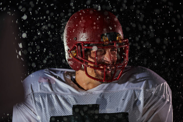 American Football Field: Lonely Athlete Warrior Standing on a Field Holds his Helmet and Ready to Play. Player Preparing to Run, Attack and Score Touchdown. Rainy Night with Dramatic Fog, Blue Light. - Foto, afbeelding