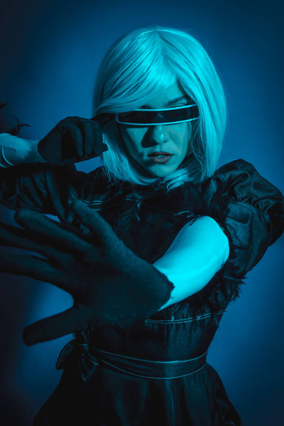 Portrait of cosplay woman in black costume and a white wig in studio with blue led light - 写真・画像