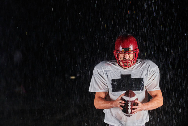 American Football Field: Lonely Athlete Warrior Standing on a Field Holds his Helmet and Ready to Play. Player Preparing to Run, Attack and Score Touchdown. Rainy Night with Dramatic Fog, Blue Light. - Фото, зображення