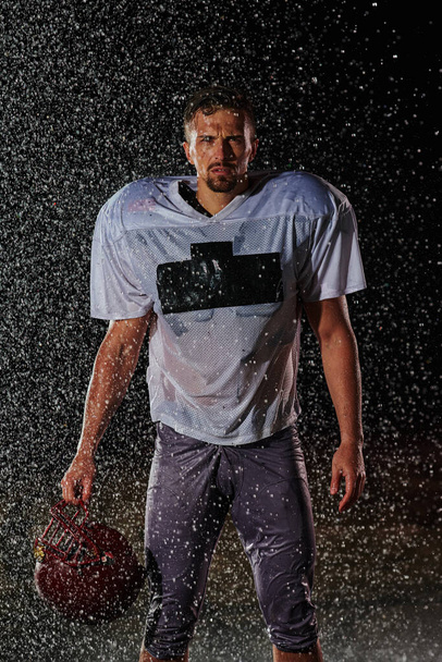 American Football Field: Lonely Athlete Warrior Standing on a Field Holds his Helmet and Ready to Play. Player Preparing to Run, Attack and Score Touchdown. Rainy Night with Dramatic Fog, Blue Light. - Foto, imagen